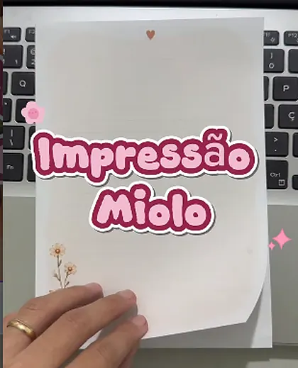 Pessoa segurando uma folha impressa com o miolo de um bloquinho diante do notebook