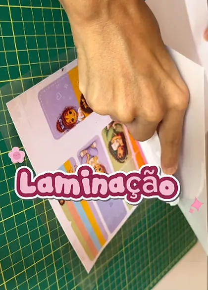 Mão posicionando folhas laminadas de bloquinhos sobre a mesa de corte verde